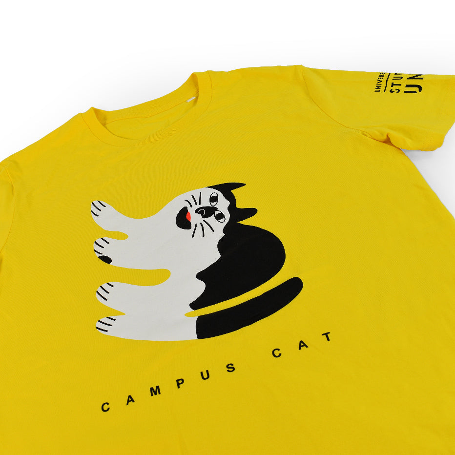 A yellow t-shirt with the words " Campus Cat" on the front and an illustration of a black and white cat printed on it, close-up on design